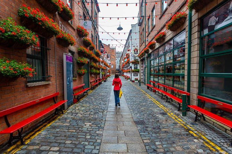 a woman walking down a narrow street with red benches Wallpaper