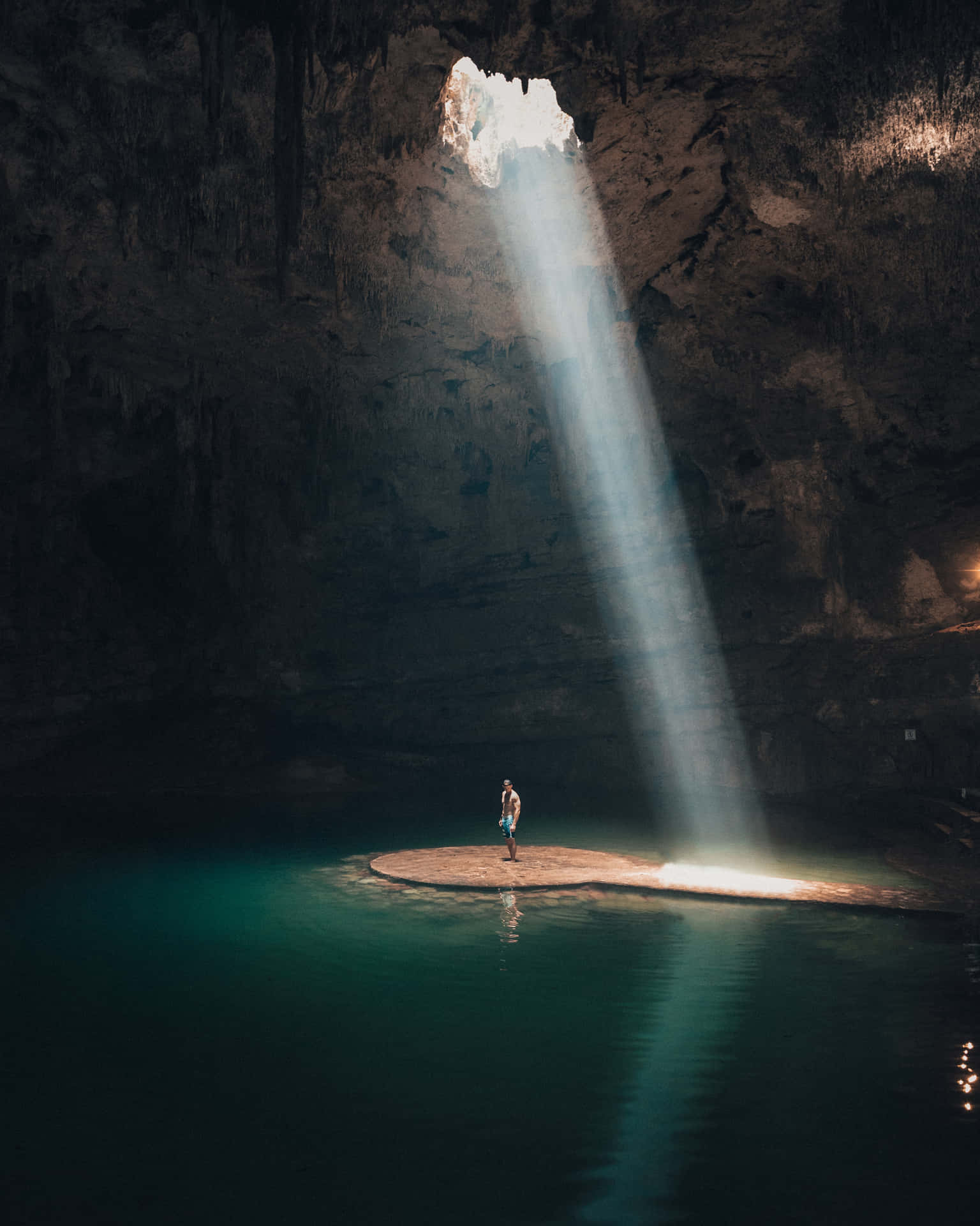 A Person Standing In A Cave With Sunlight Shining Through The Water
