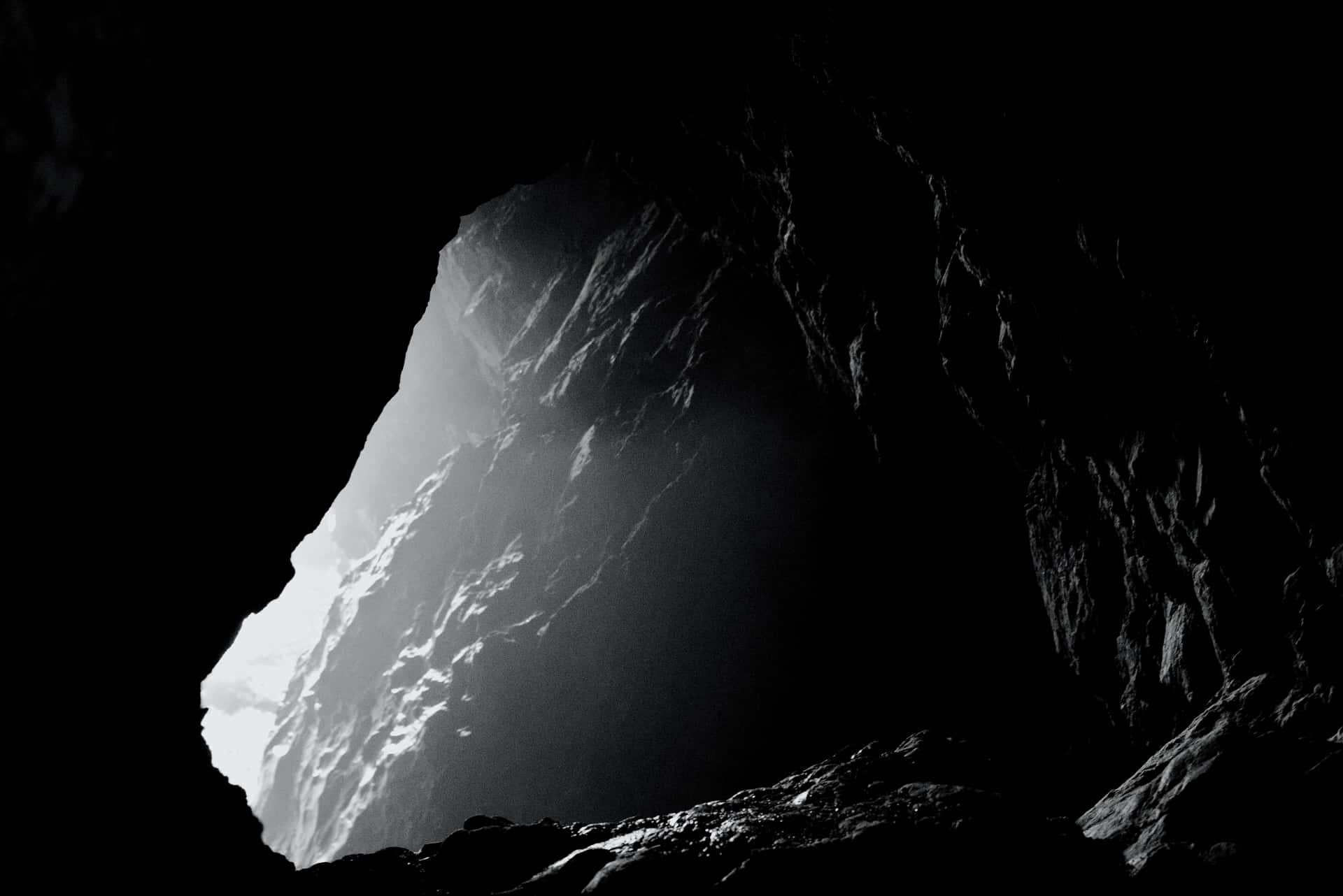 A Black And White Photo Of A Cave With A Light Shining Through