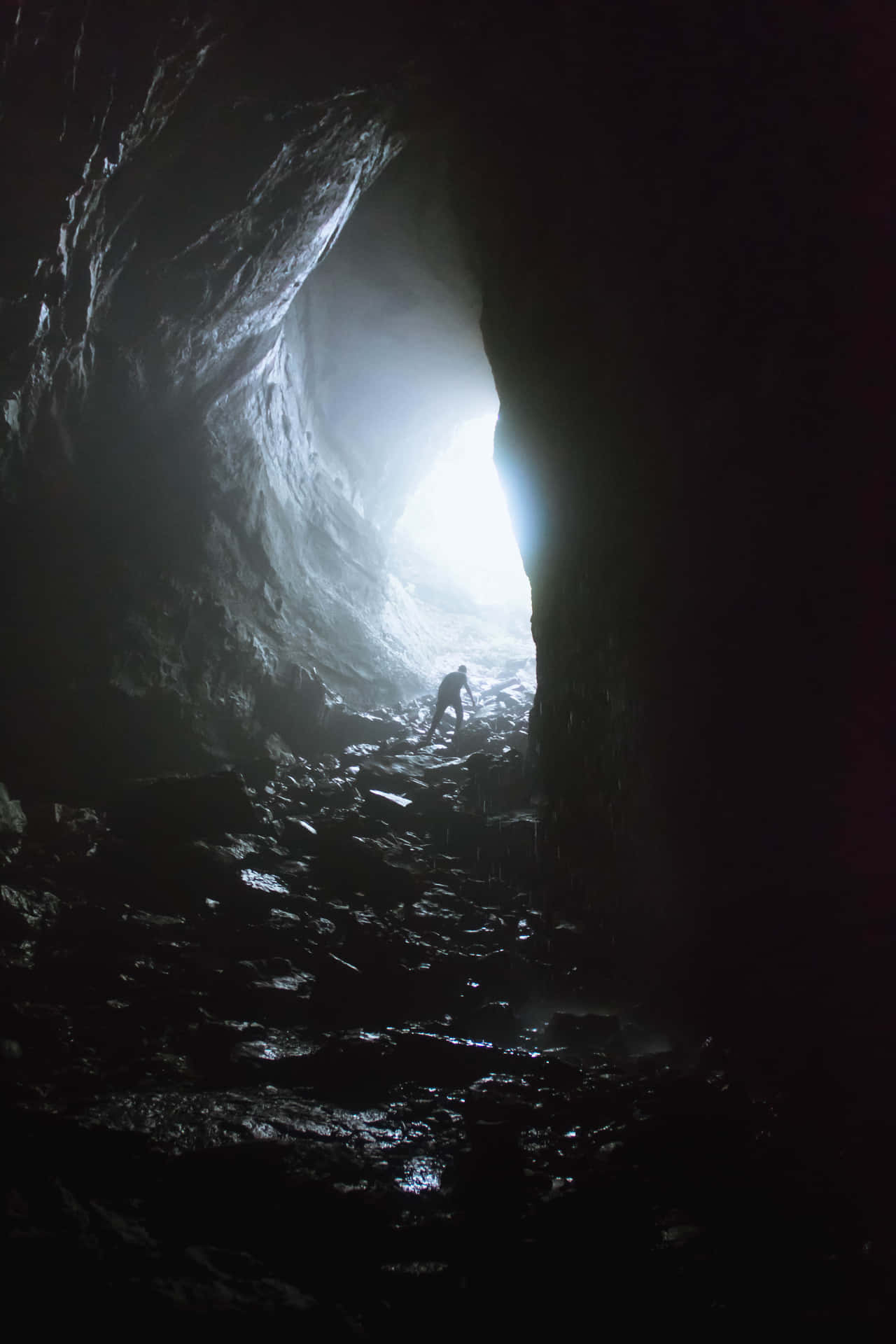 A Man Is Standing In A Cave With Light Coming Out Of It
