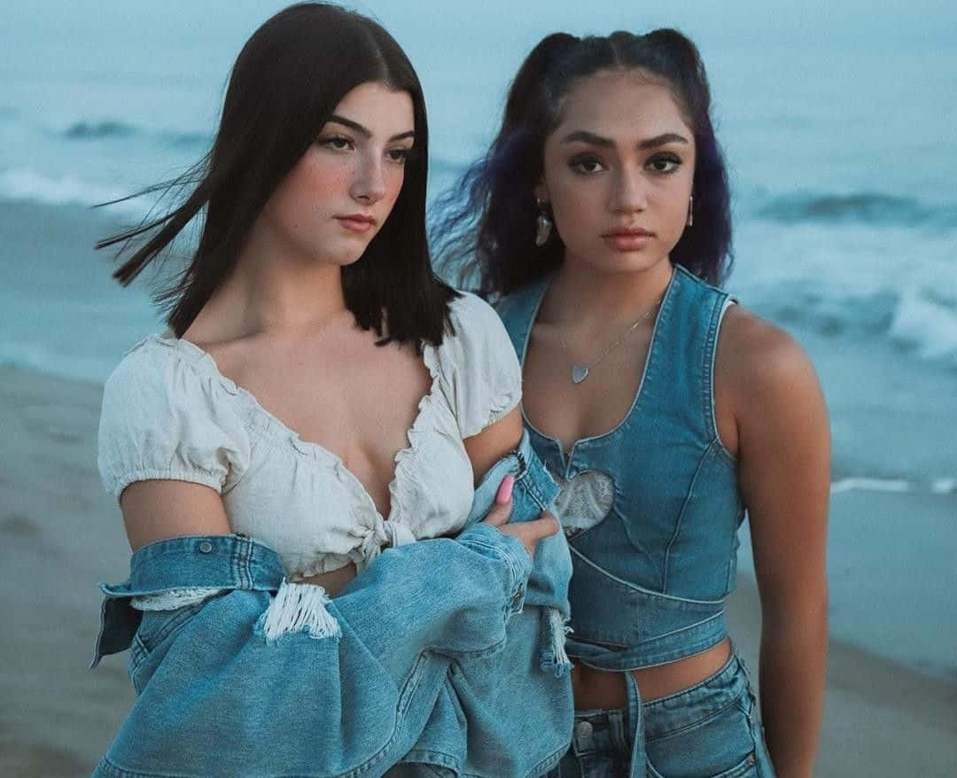 To kvinder står på stranden iført denim jeans. Wallpaper