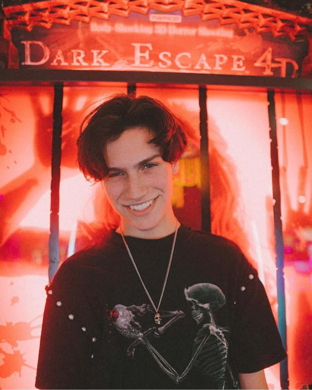 A Young Man Smiling In Front Of A Dark Escape Sign Wallpaper