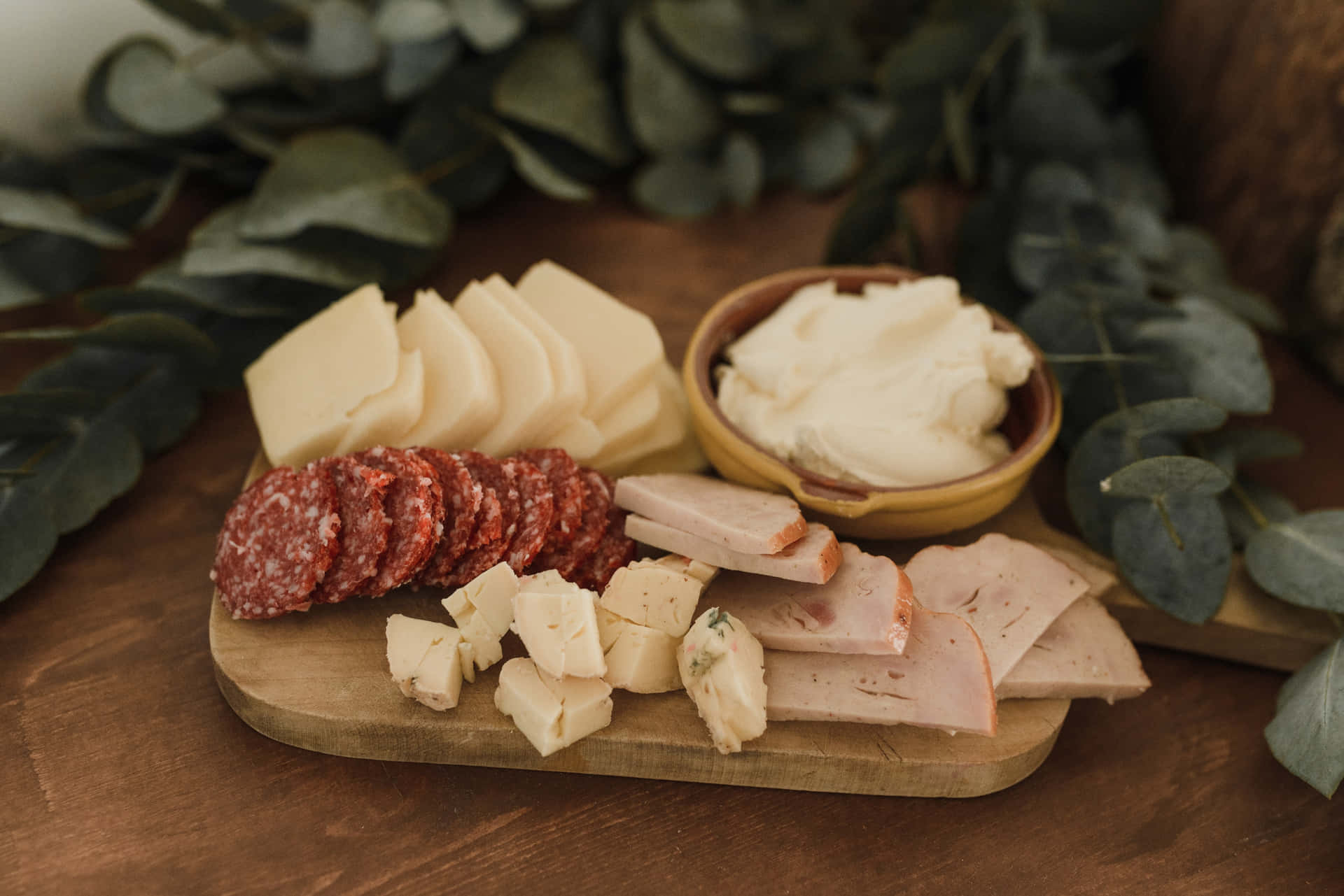 Assorted Cheeses on Wooden Platter and Green Leafy Background