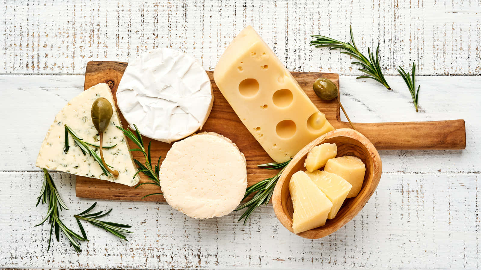 A Wooden Board With Cheese, Olives And Rosemary