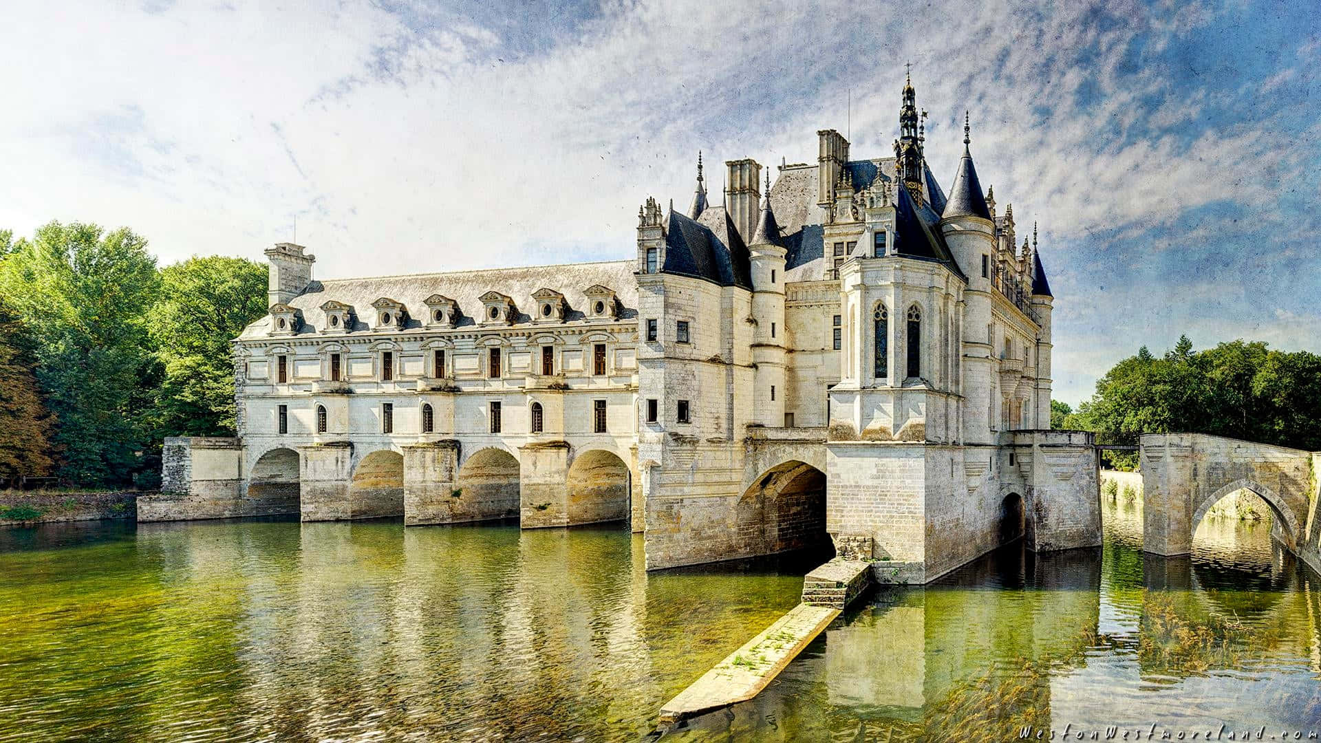 Caption: "Scenic View of Majestic Chenonceau Castle Over Mossy Water" Wallpaper