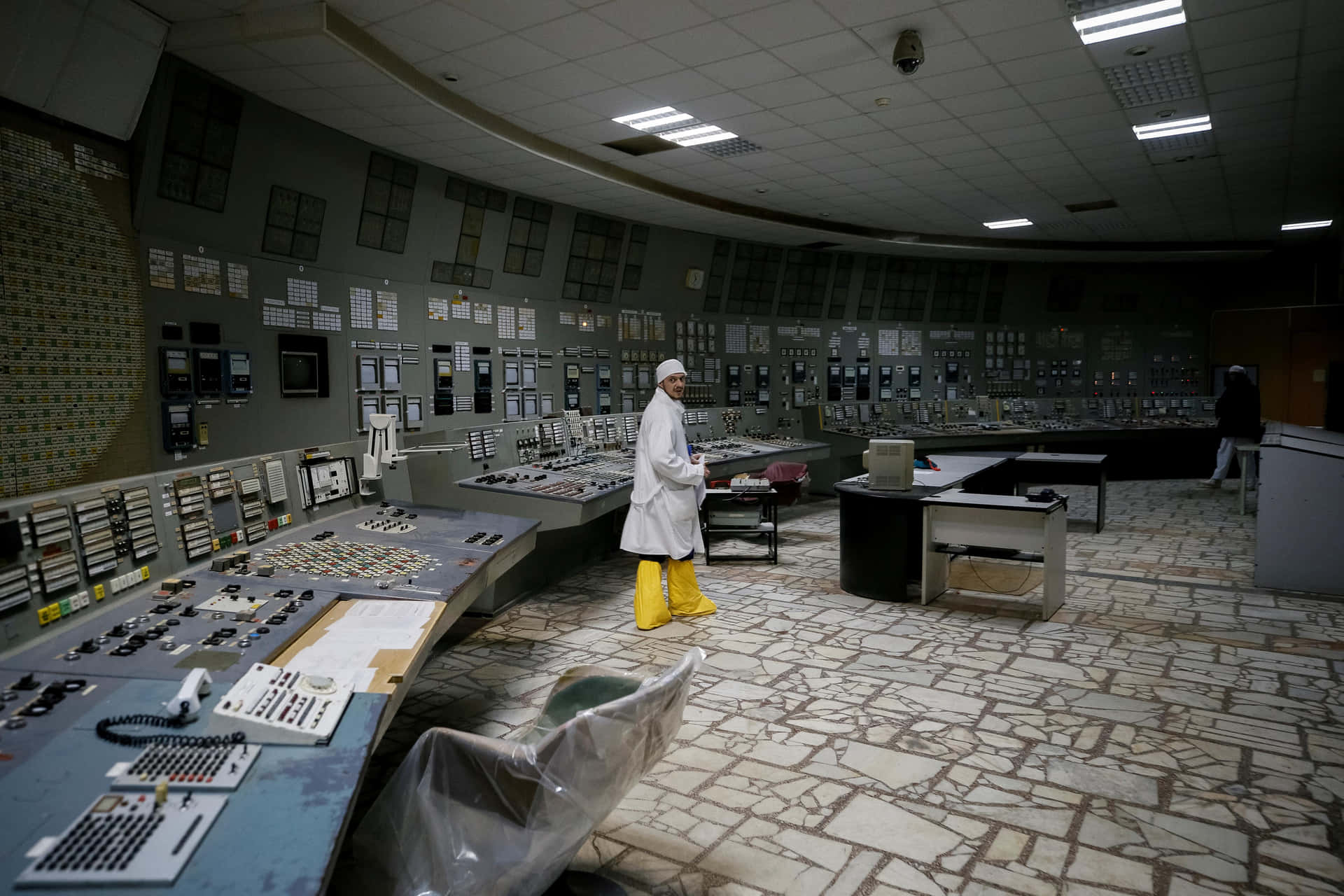 A Worker In A Protective Suit Stands In A Control Room