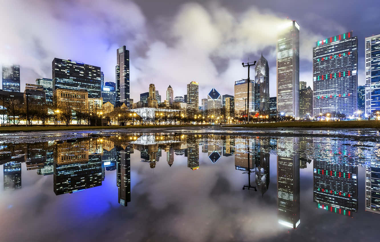 Et billede af Chicagos skyline spejlet i en sø om natten Wallpaper