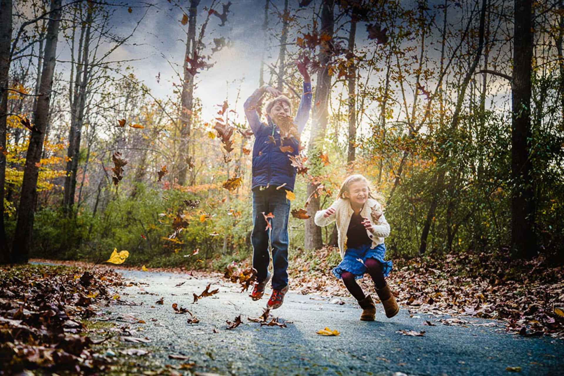 Two Children Are Jumping In The Air While Throwing Leaves