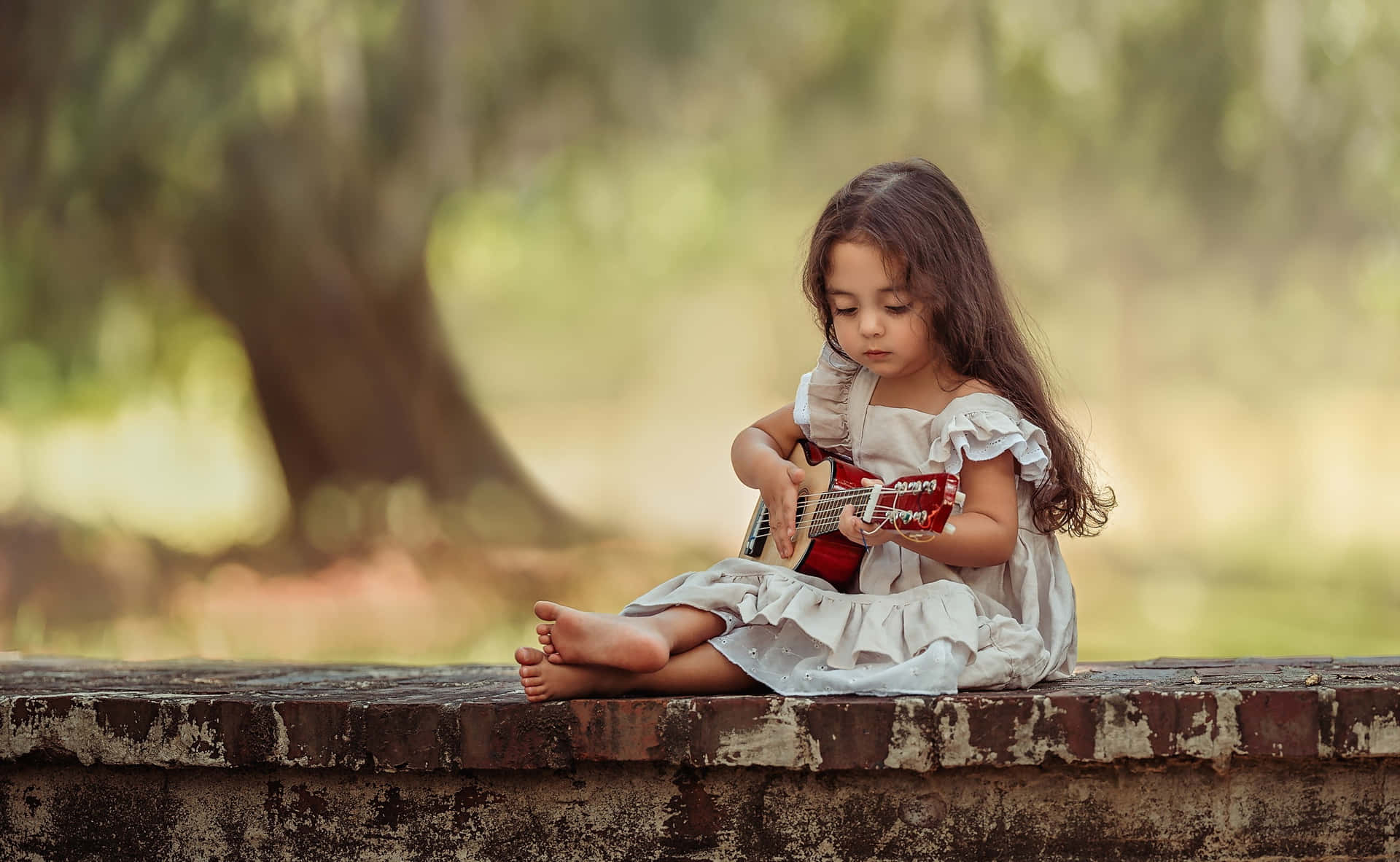 Einkleines Mädchen Sitzt Auf Einer Ziegelmauer Und Spielt Gitarre.