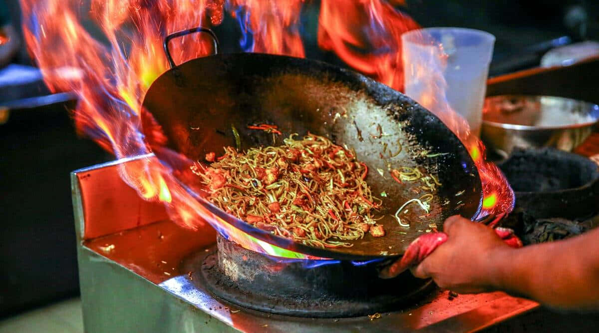 A Person Is Cooking Food In A Wok On Fire