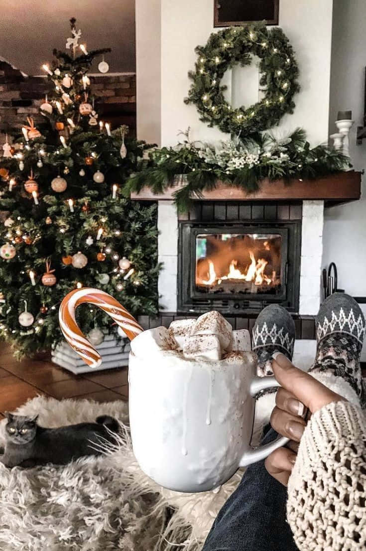 A Person Is Sitting In Front Of A Fireplace With A Cup Of Hot Cocoa