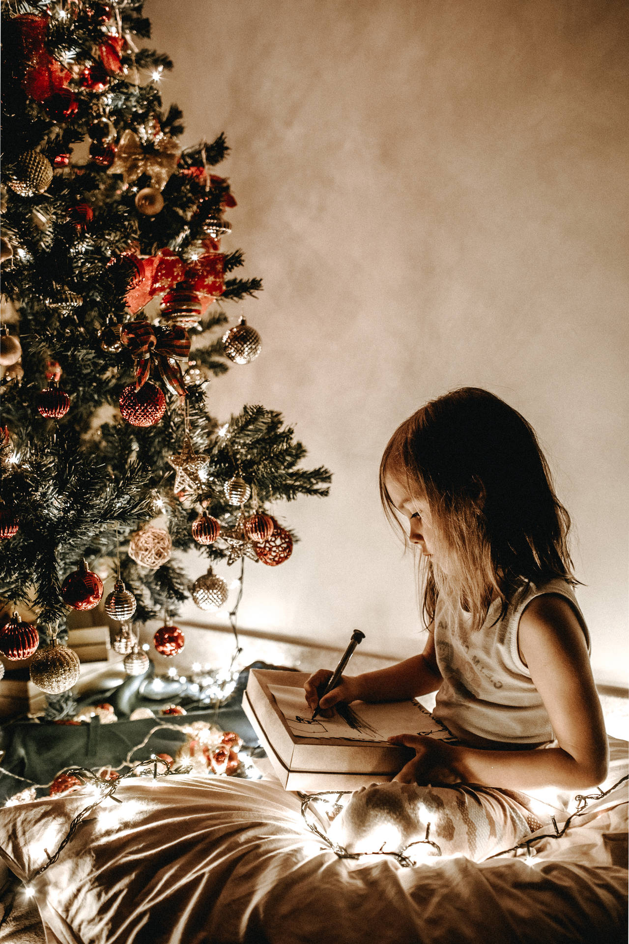 Girl writing on her present by a Christmas tree wallpaper.