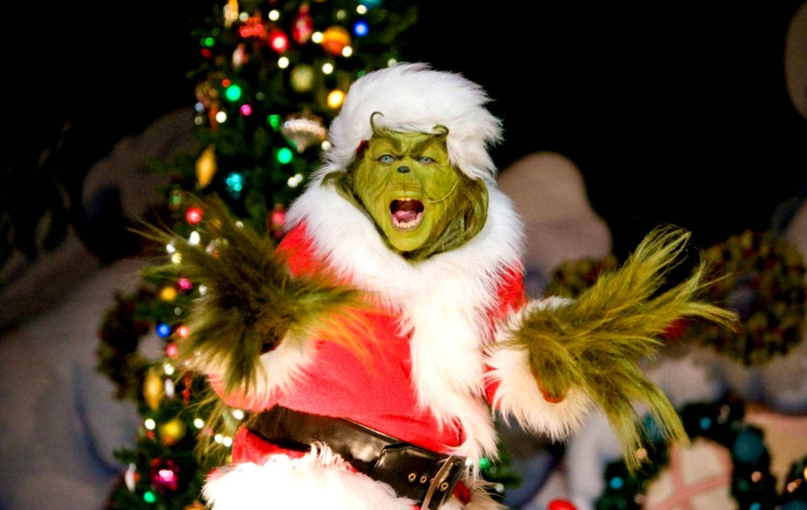 A Man Dressed As The Grinch Is Performing In Front Of A Christmas Tree Wallpaper