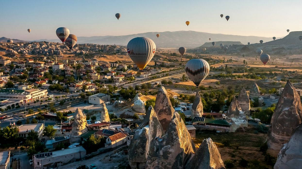 Hot Air Balloons Flying Over A Town Wallpaper