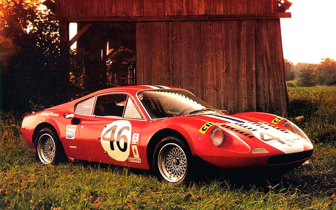 A Red Race Car Parked In Front Of A Barn Wallpaper
