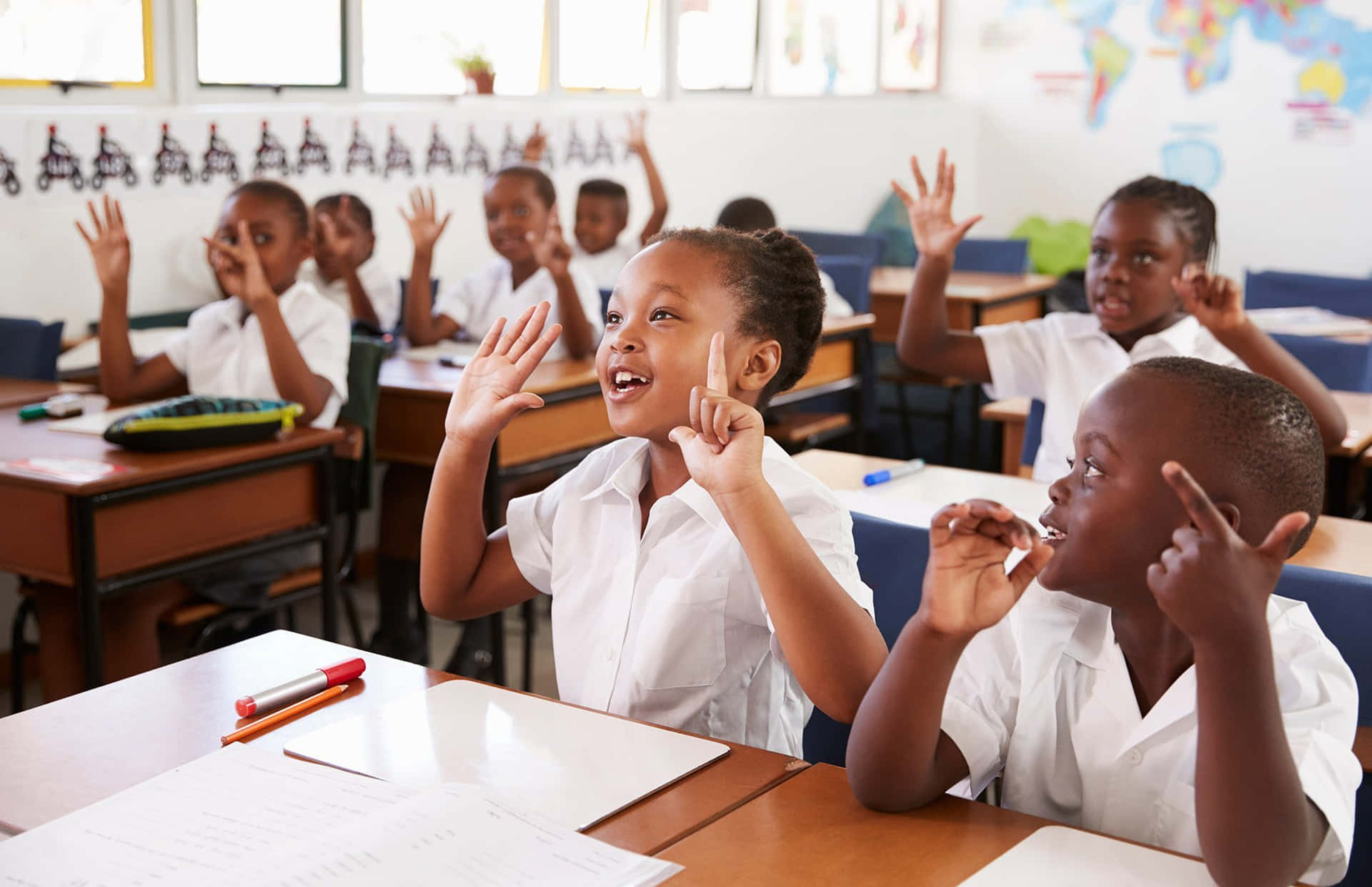 Children In A Classroom Raising Their Hands