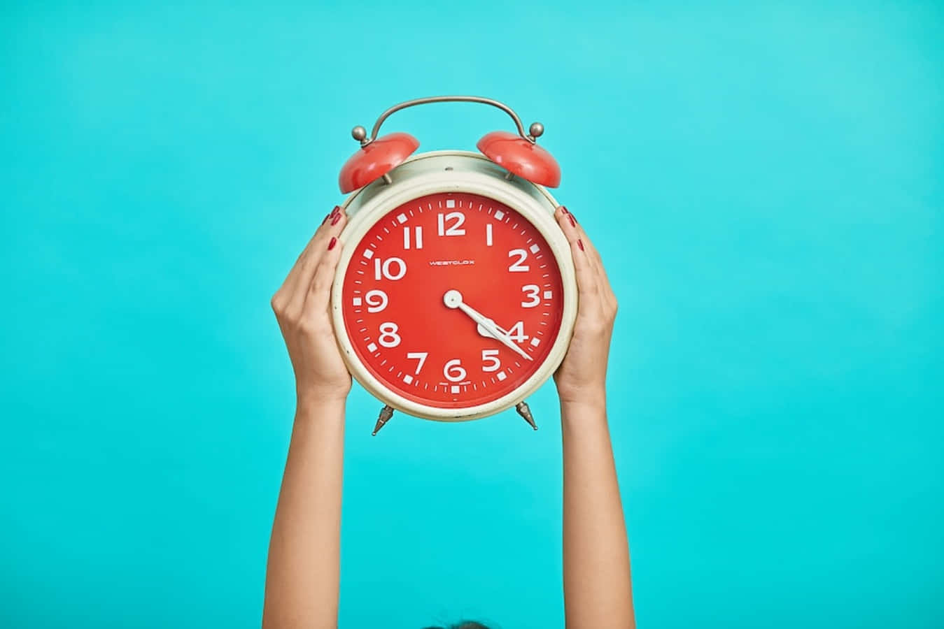 Woman Holding Up Alarm Clock On Blue Background
