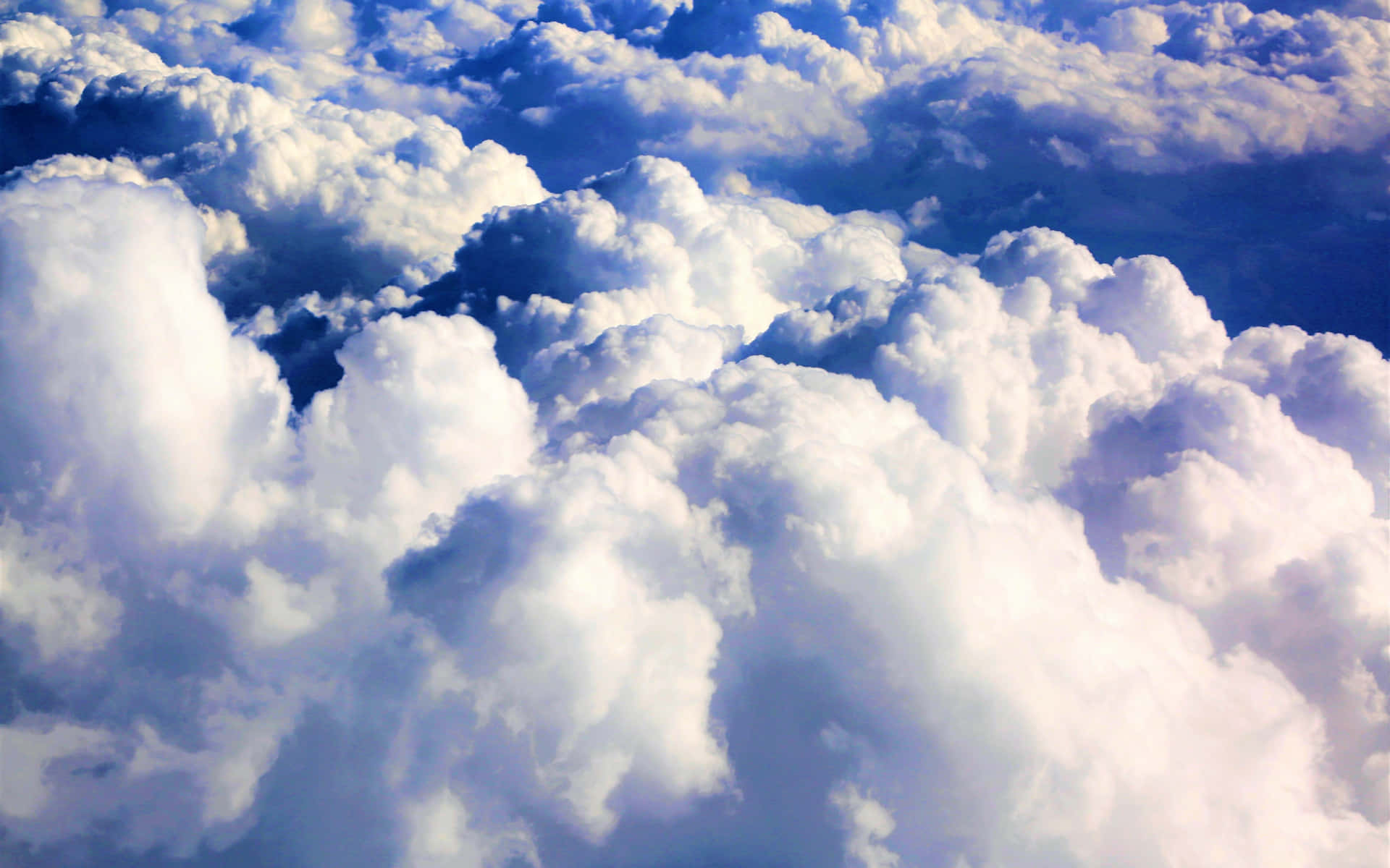 A majestic aerial view of fluffy clouds in a vibrant blue sky. Wallpaper