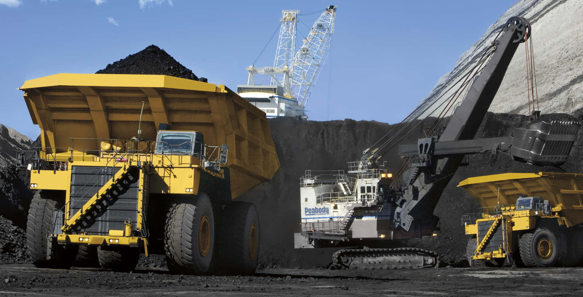 A Group Of Trucks And A Crane In Front Of A Coal Field