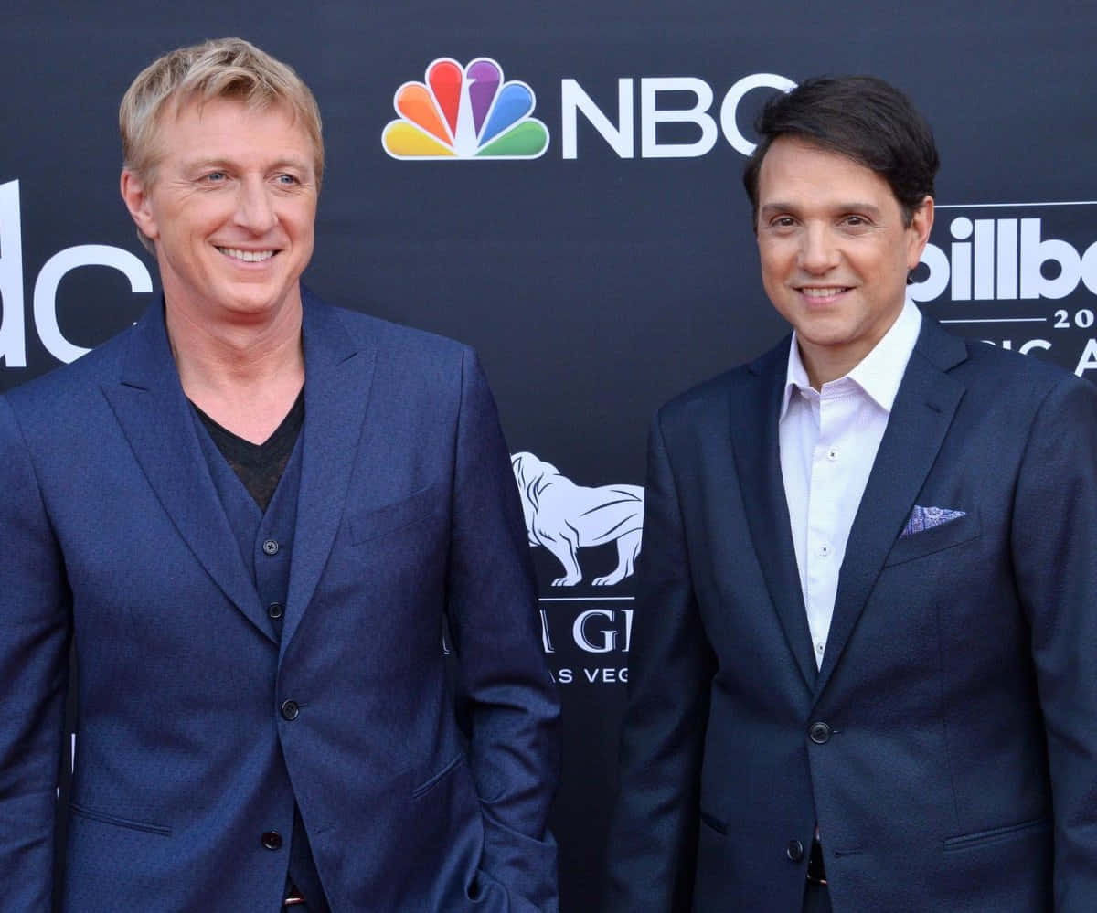 Two Men In Suits Standing On A Red Carpet