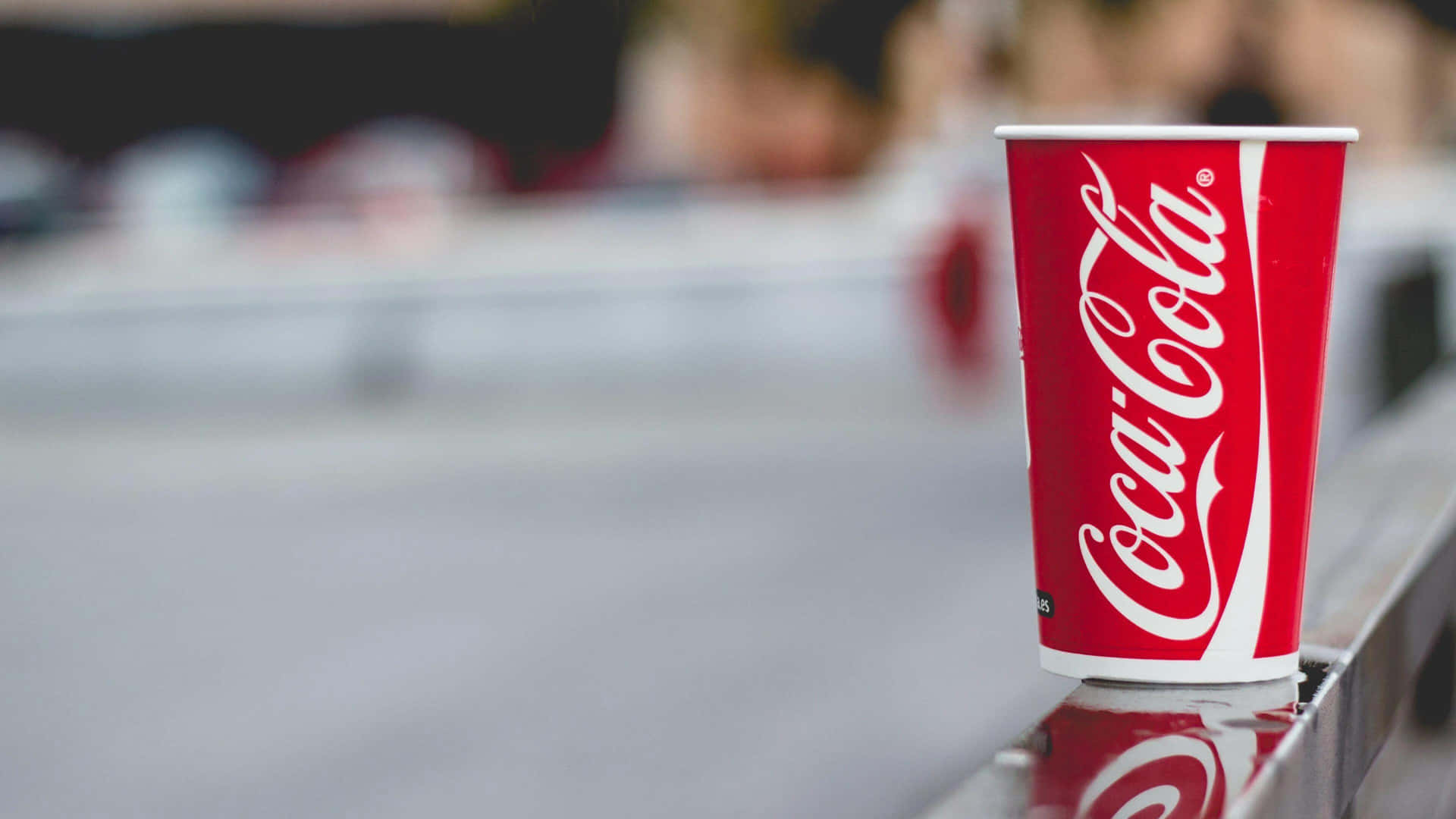 A Coca Cola Cup Sits On A Railing