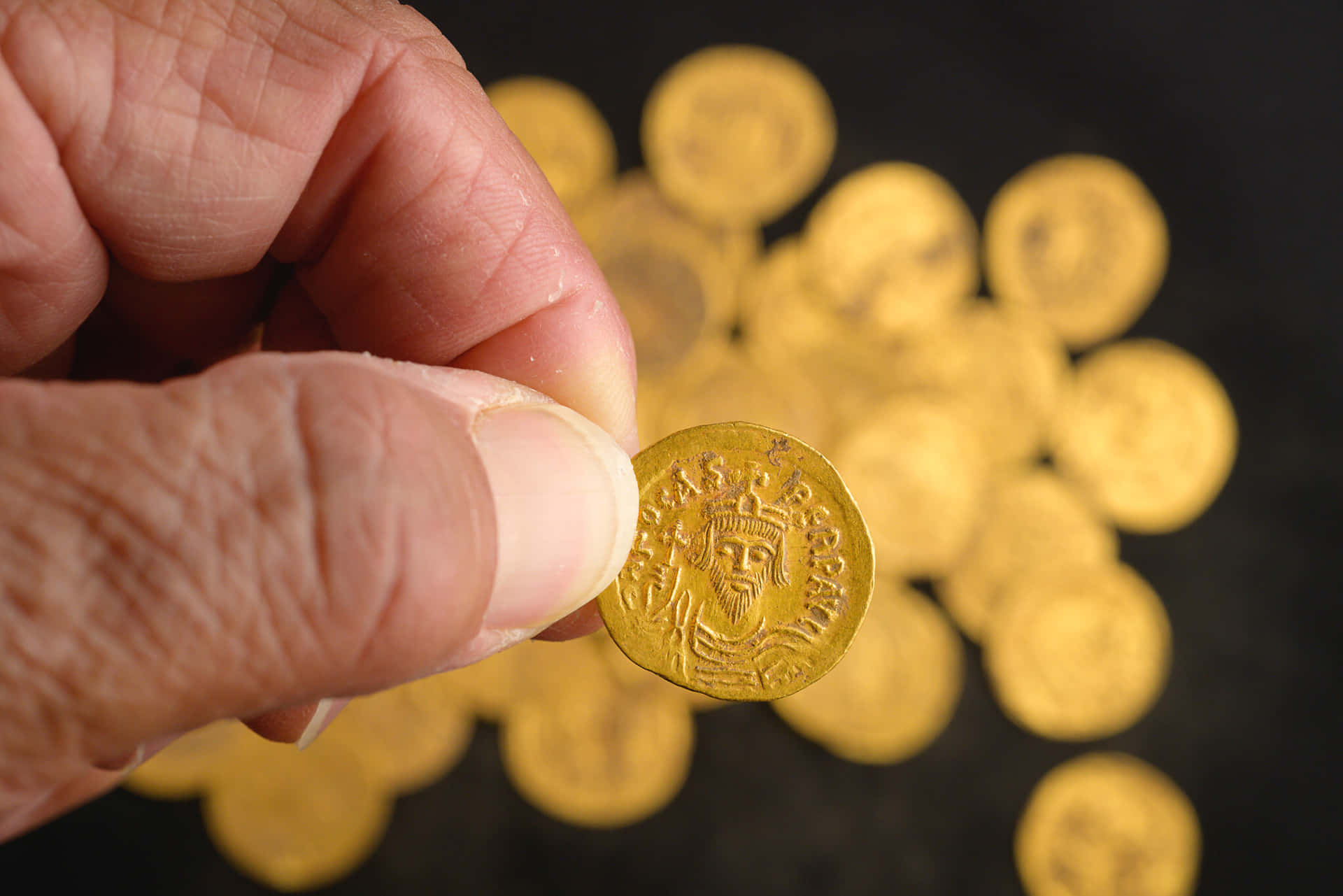 A Person Holding A Gold Coin In Front Of A Black Background