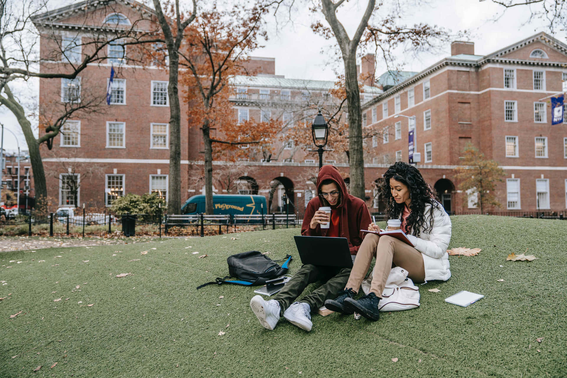 Two Students Sitting On The Grass With Laptops
