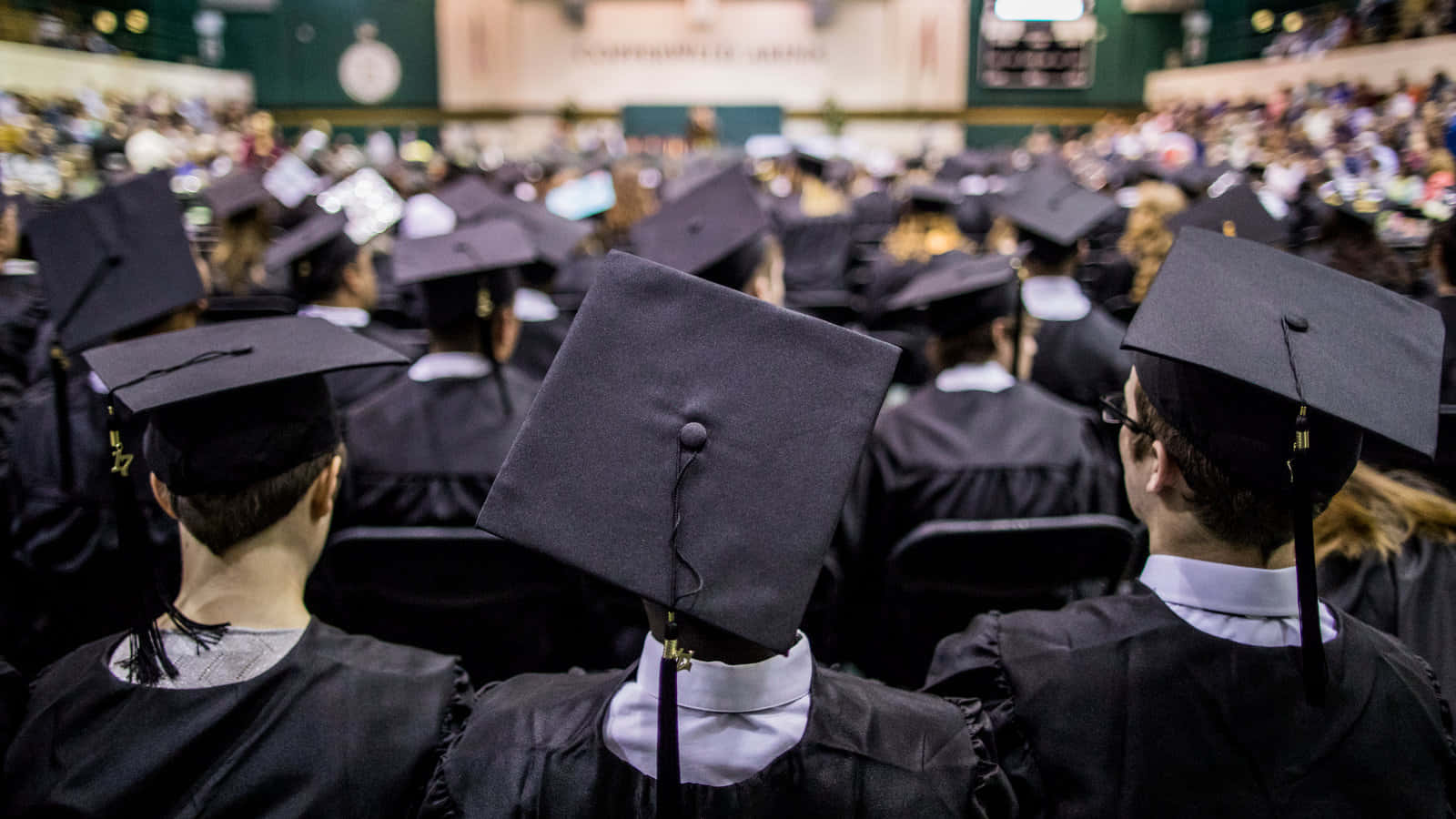 Graduates In Black Hats Are Sitting In A Large Auditorium