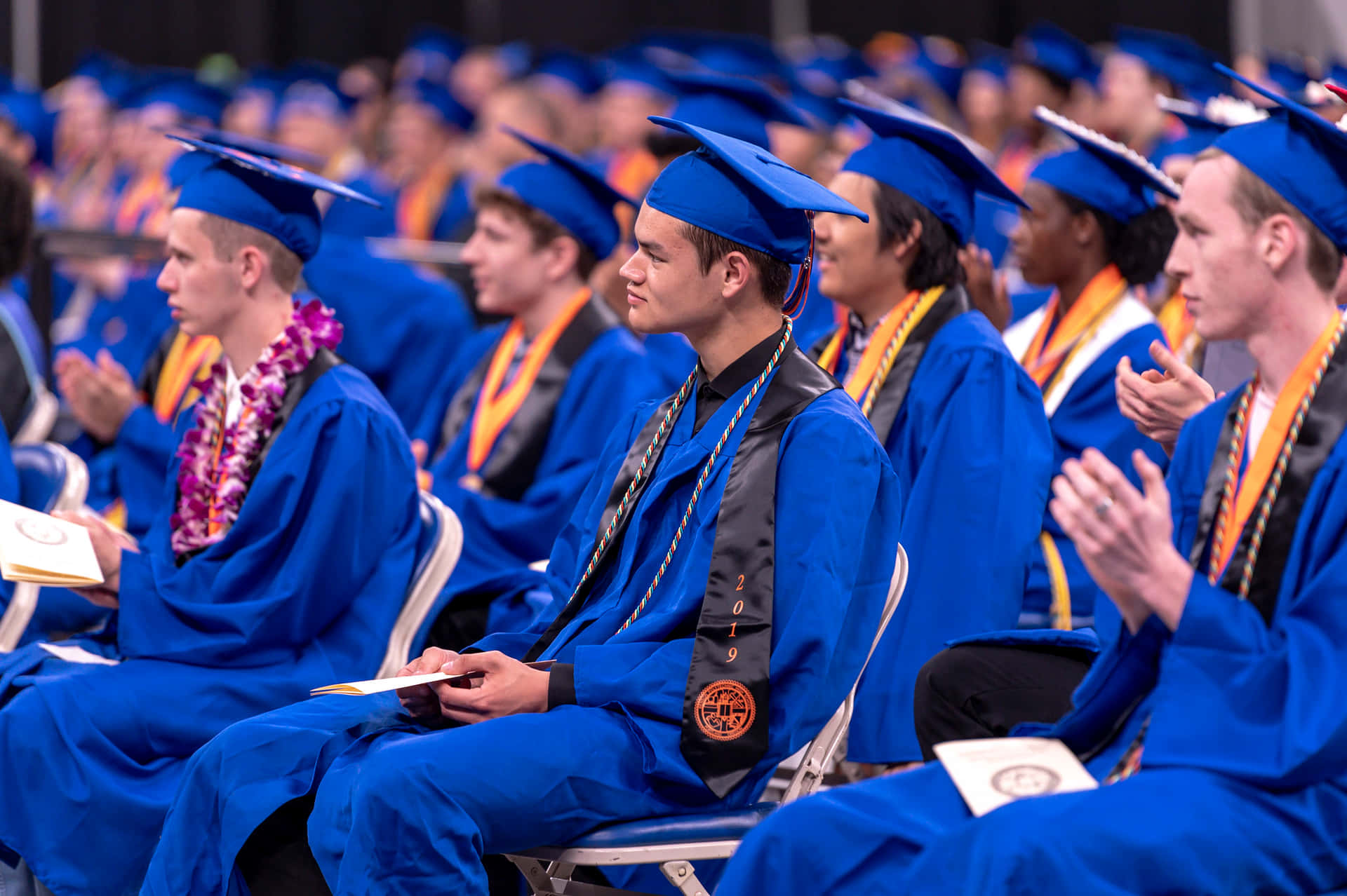 En gruppe af afgangsstuderende i blå kapper klapper på et podie.