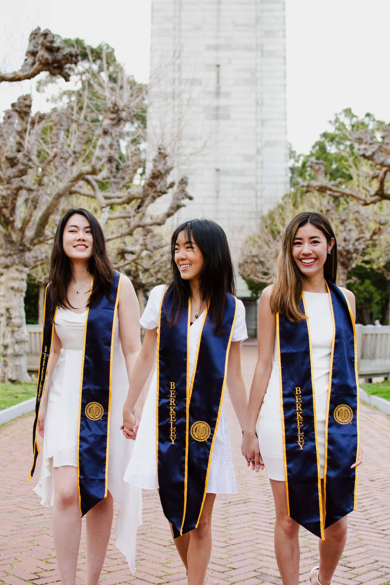 Tre kvinder iført eksamenskjoler, der holder i hænderne.