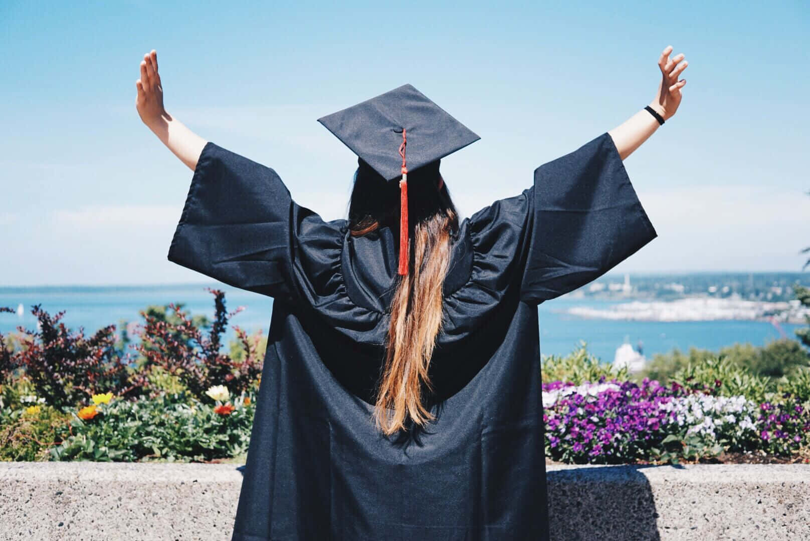 A Woman In A Graduation Gown With Her Arms Raised
