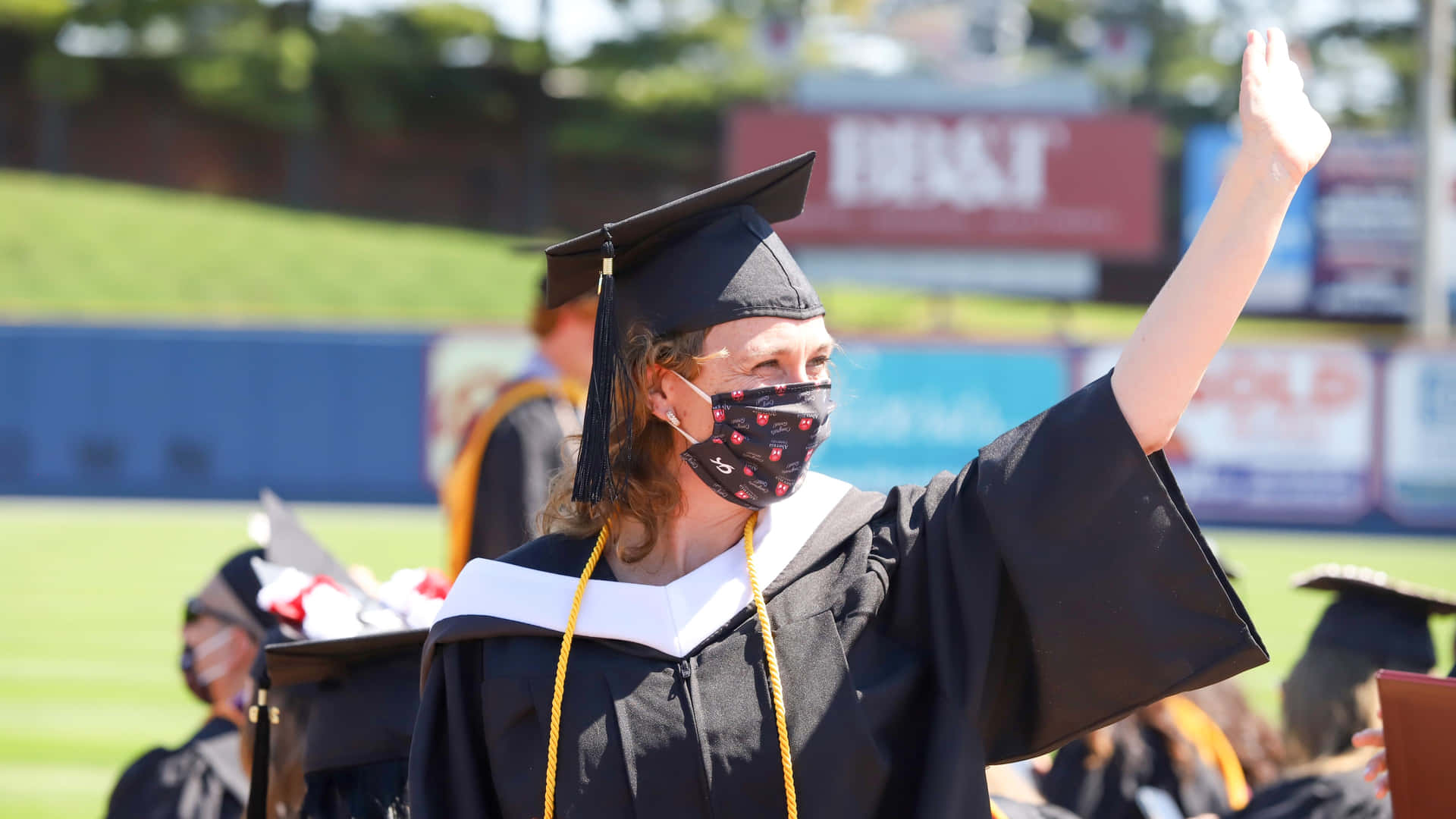 A Woman In Graduation Gown Waves To The Crowd