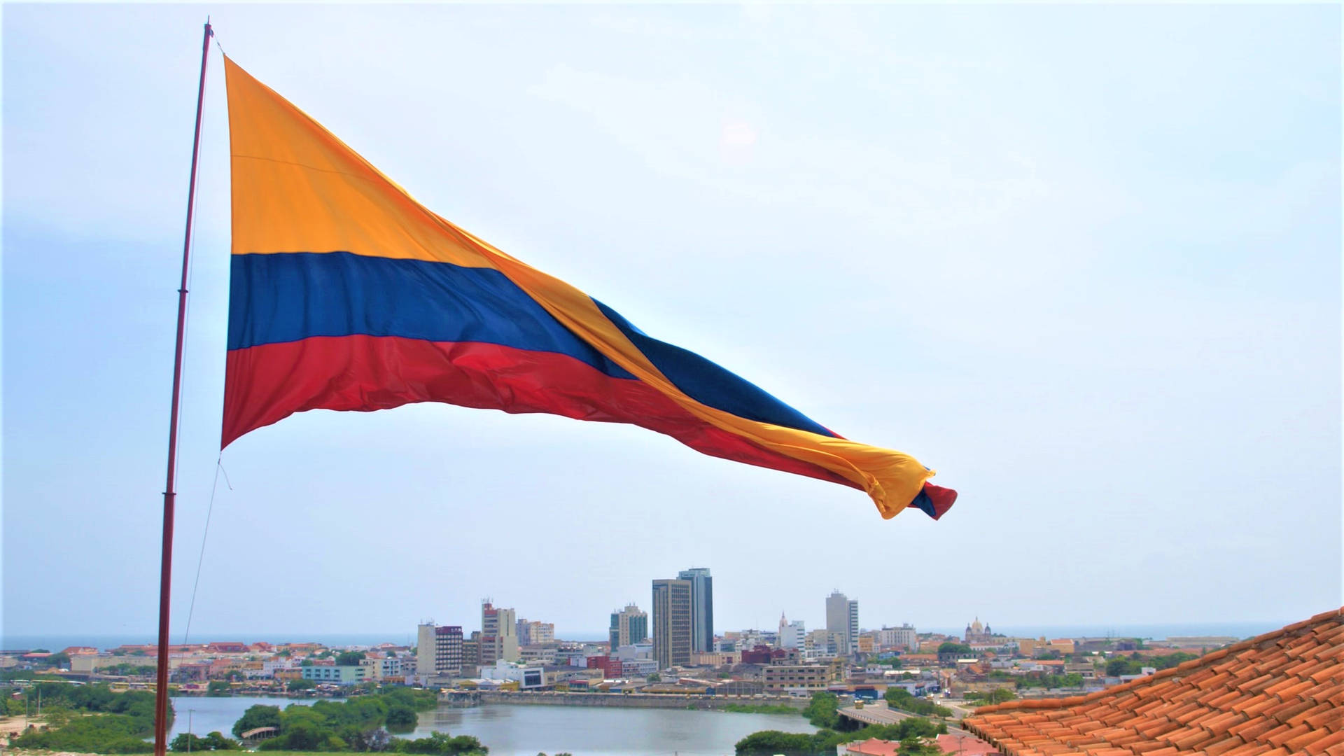 Caption: Vibrant Colombian flag waving proudly over a bustling cityscape. Wallpaper