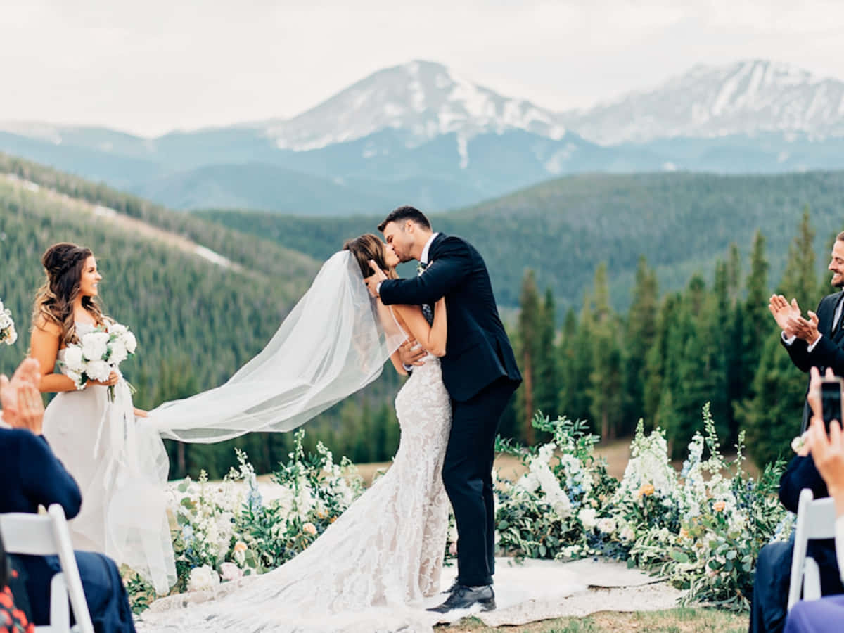 A Bride And Groom Kissing In Front Of Mountains