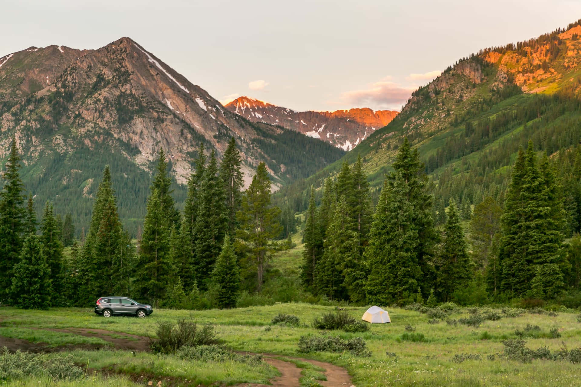 A Camper Is Parked In The Middle Of A Field With Mountains In The Background