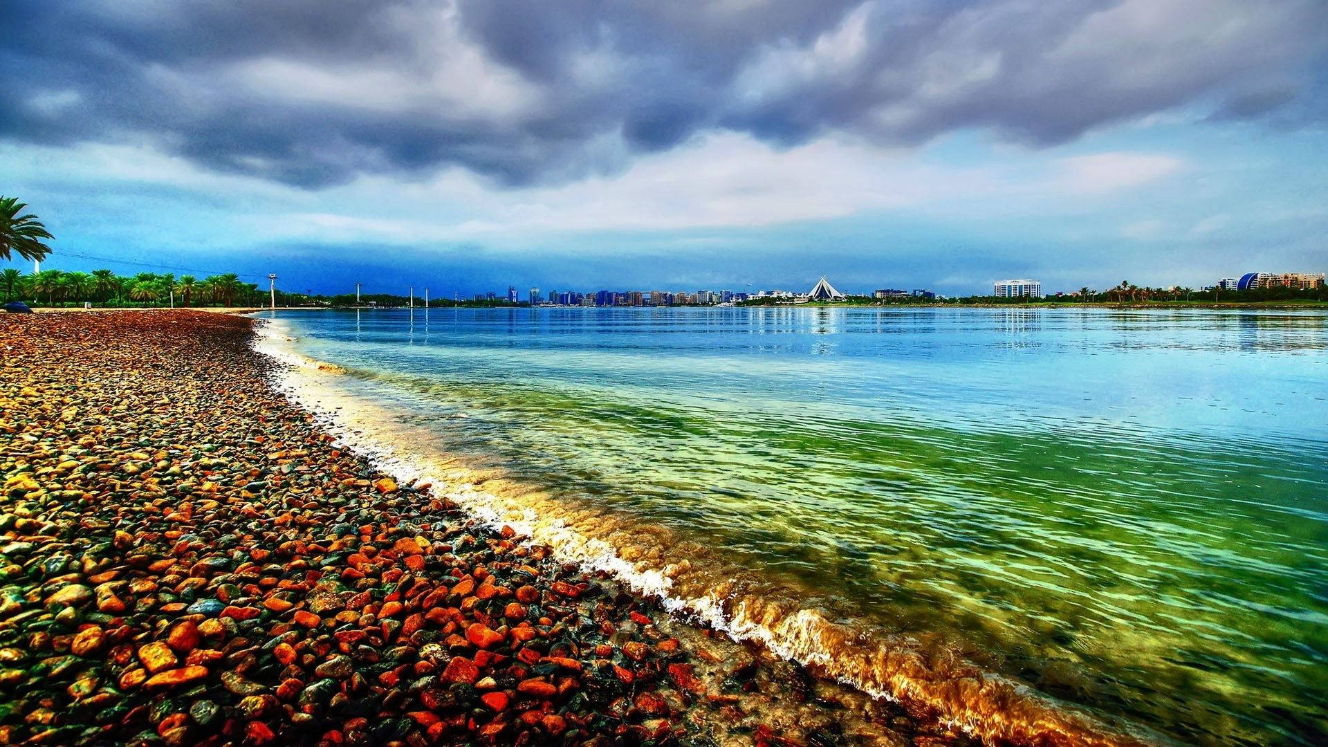 Seagrass between waves of colorful gravel along the shoreline of a beach. Wallpaper