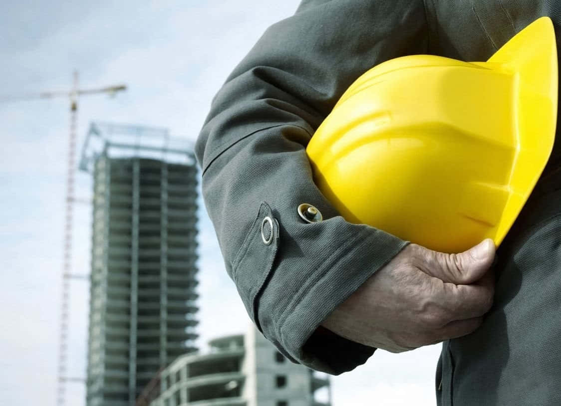 A Man Holding A Yellow Hard Hat In Front Of A Construction Site