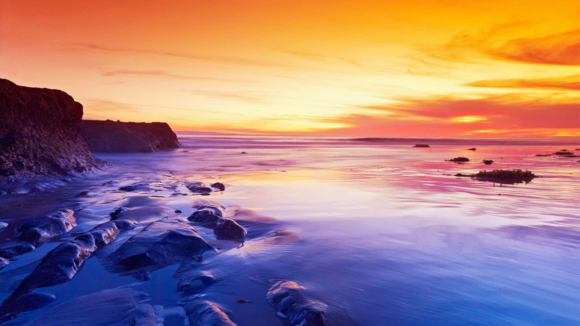 A Colorful Sunset Over The Ocean And Rocks Wallpaper