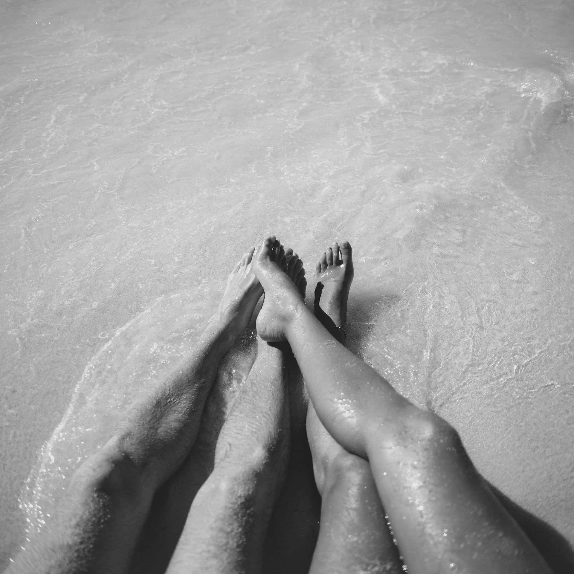 Skriv denne sætning på dansk: Et par på stranden ben sort og hvid fotografi Wallpaper
