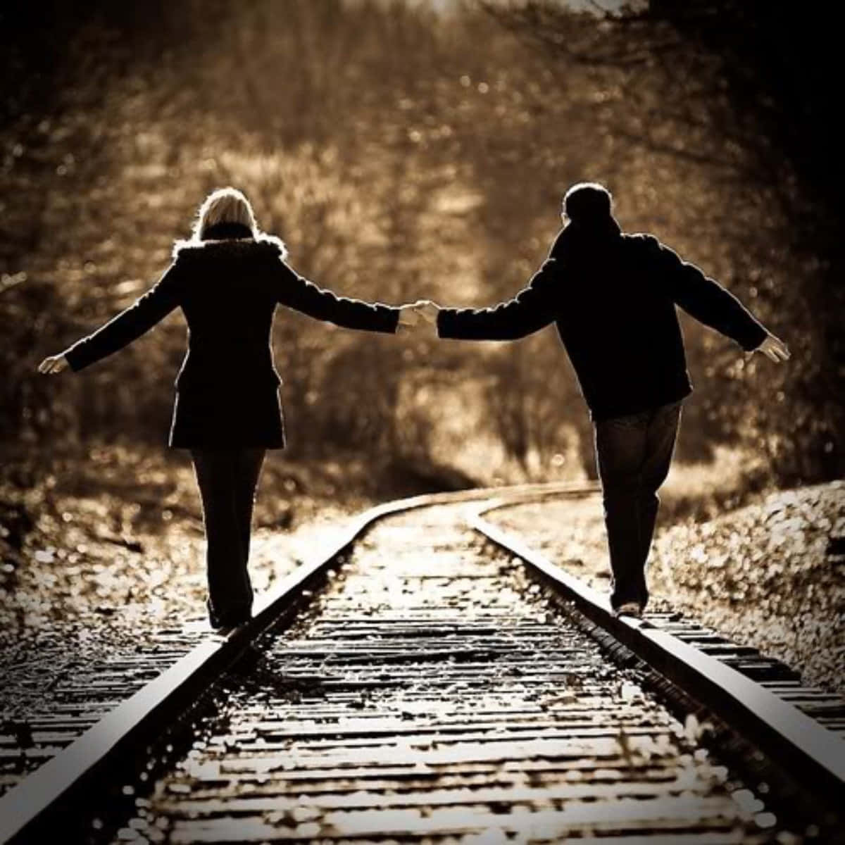 Et par går på togskinner og holder hænderne billede