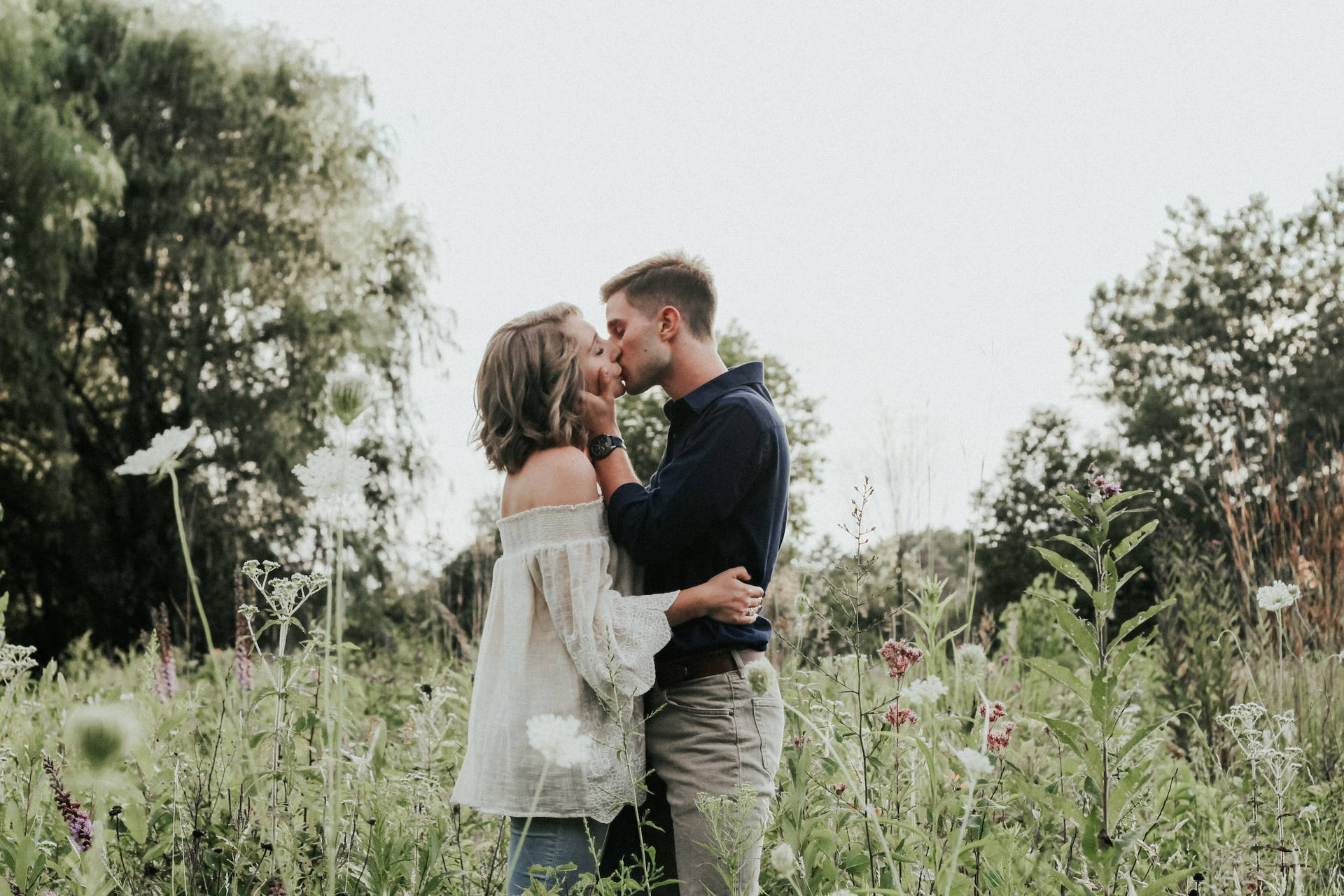 Couple Hugging And Kissing On Grassy Field Wallpaper