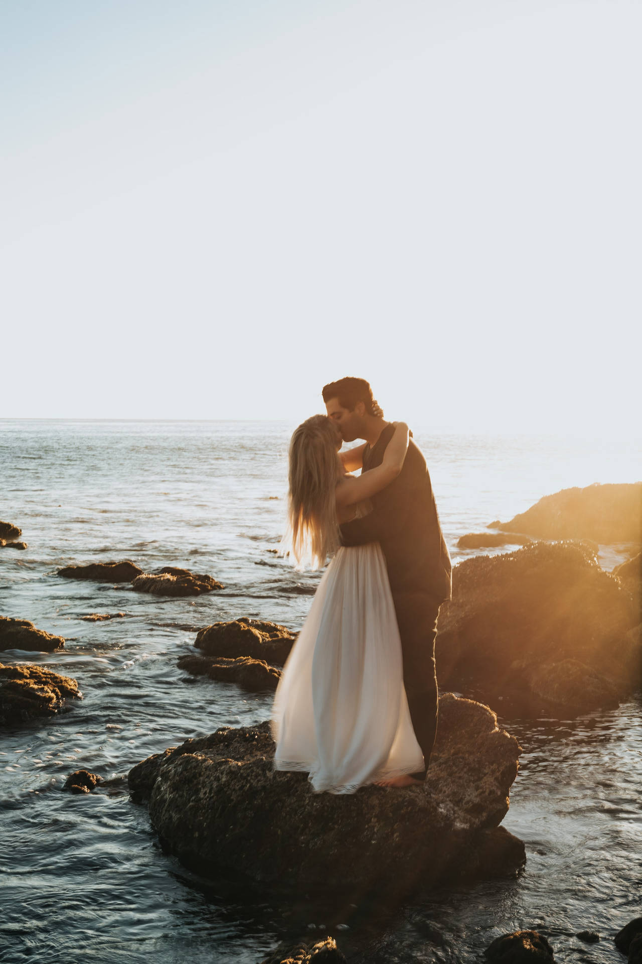 Par kramme og kysse på klippe ved havet Wallpaper