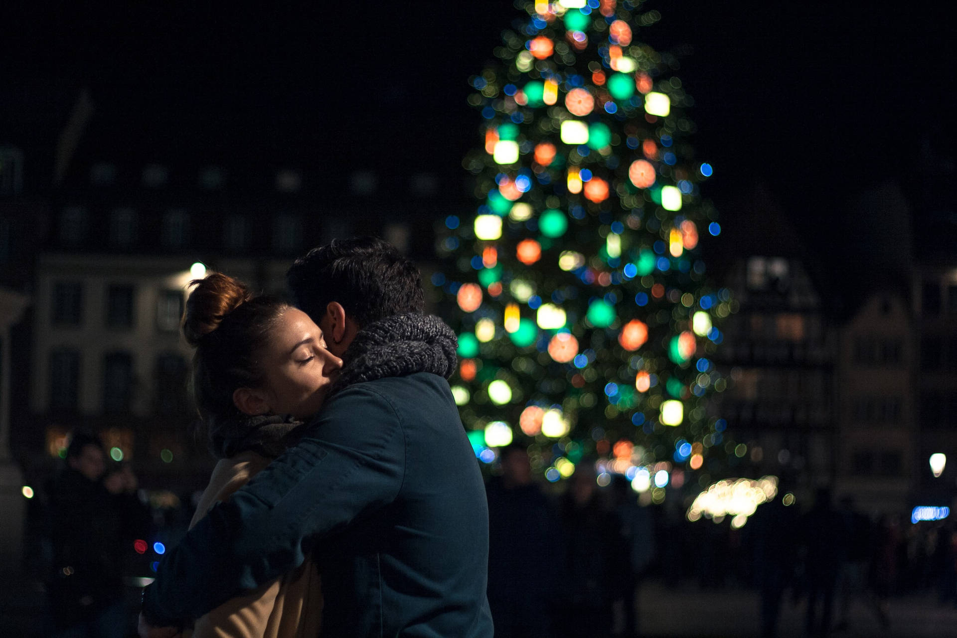Couple Hugging By A Christmas Tree Wallpaper