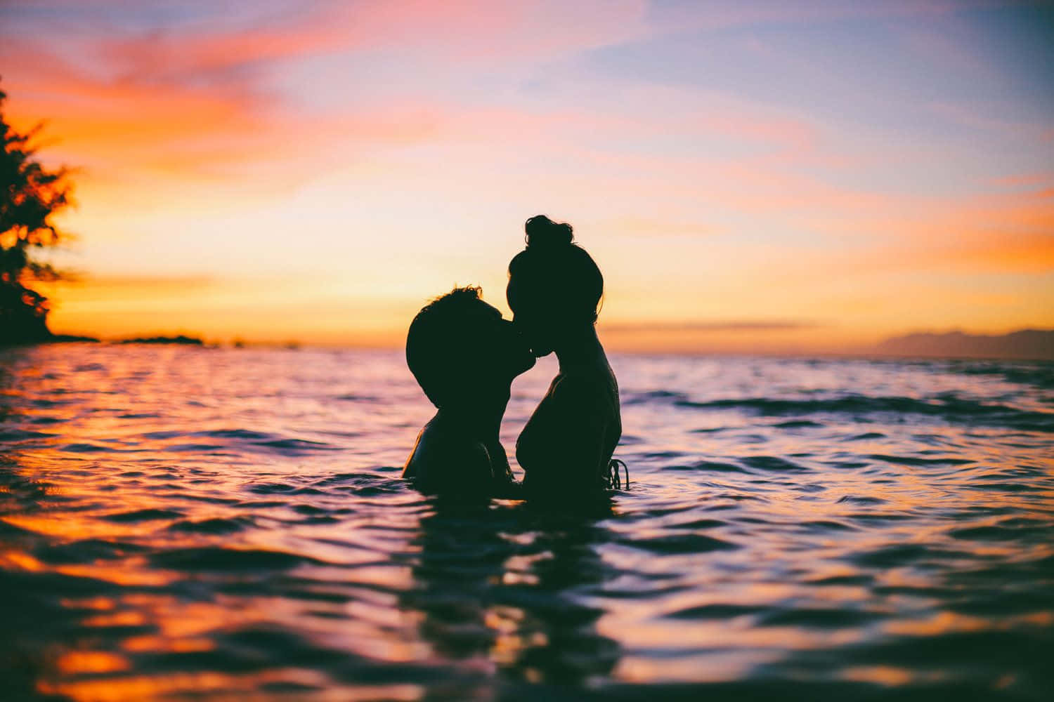 Par kysse i solnedgang på vandbillede