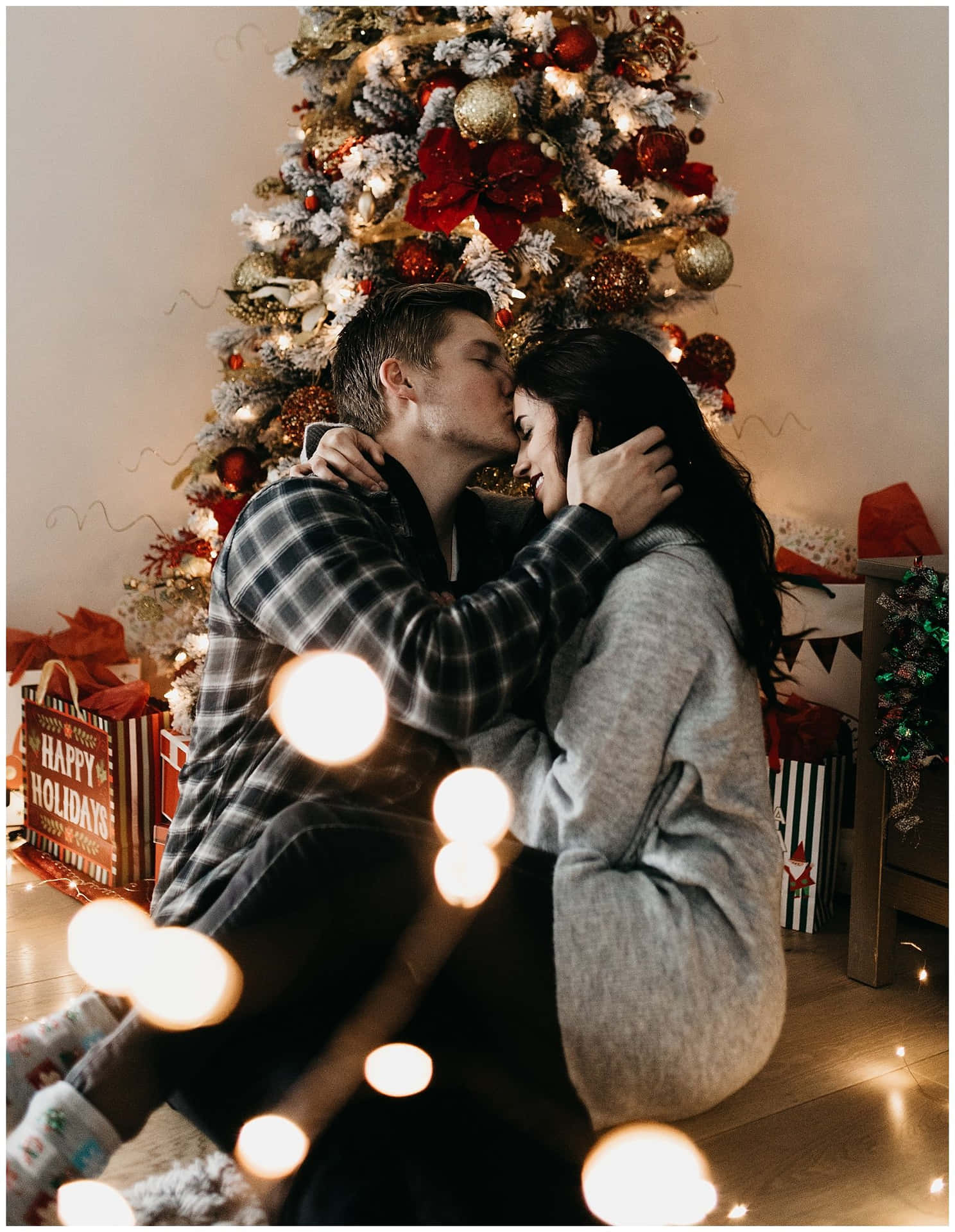 A Couple Kissing In Front Of A Christmas Tree