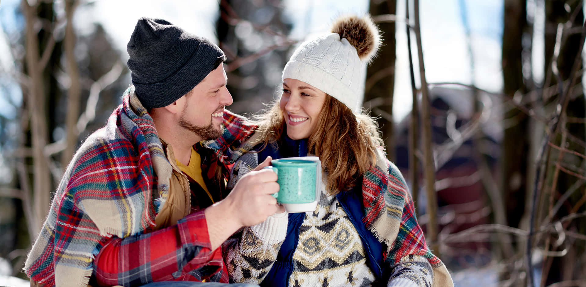 A Couple Sitting In The Snow Holding A Cup Of Coffee