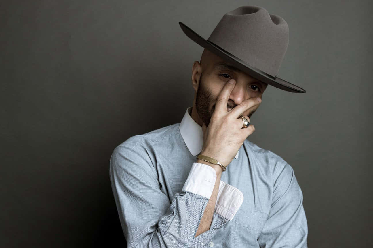 A Man In A Hat Is Posing With His Hand On His Face