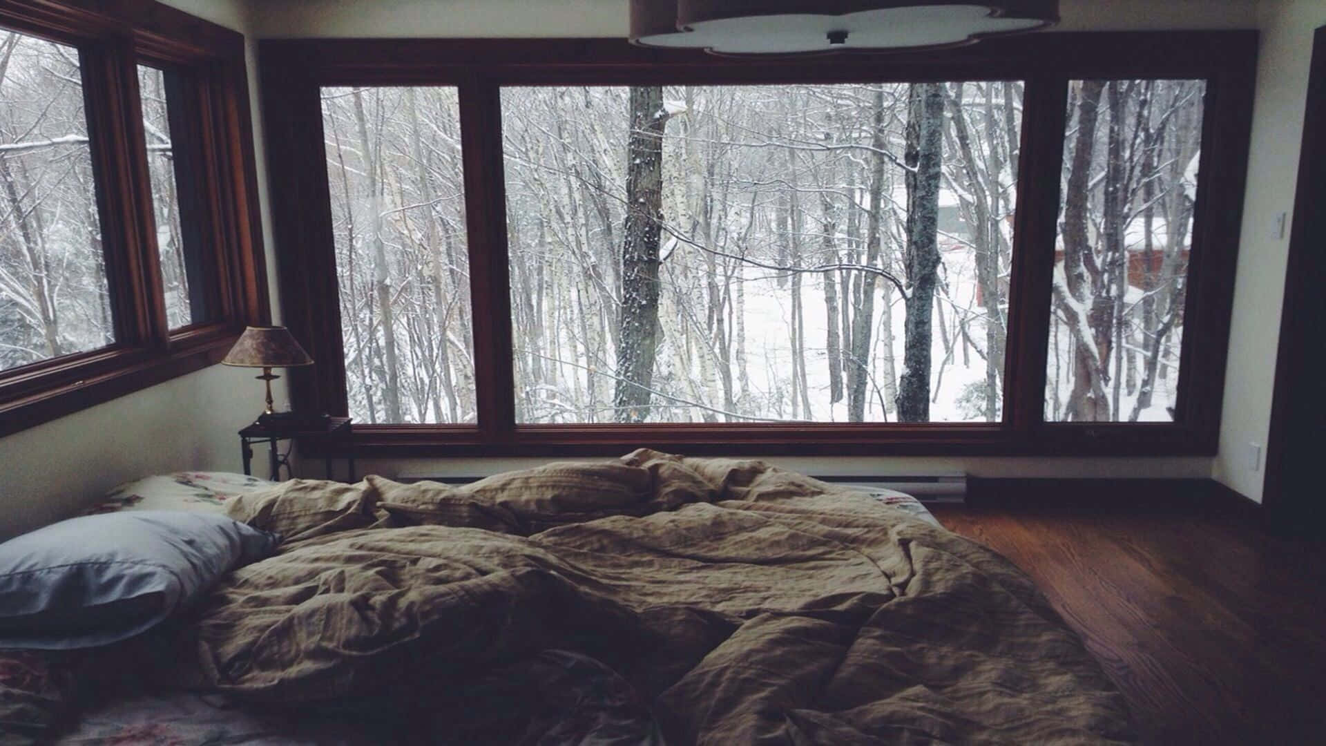 Et seng med tæppe på og et vindue med udsigt til en skov. Wallpaper
