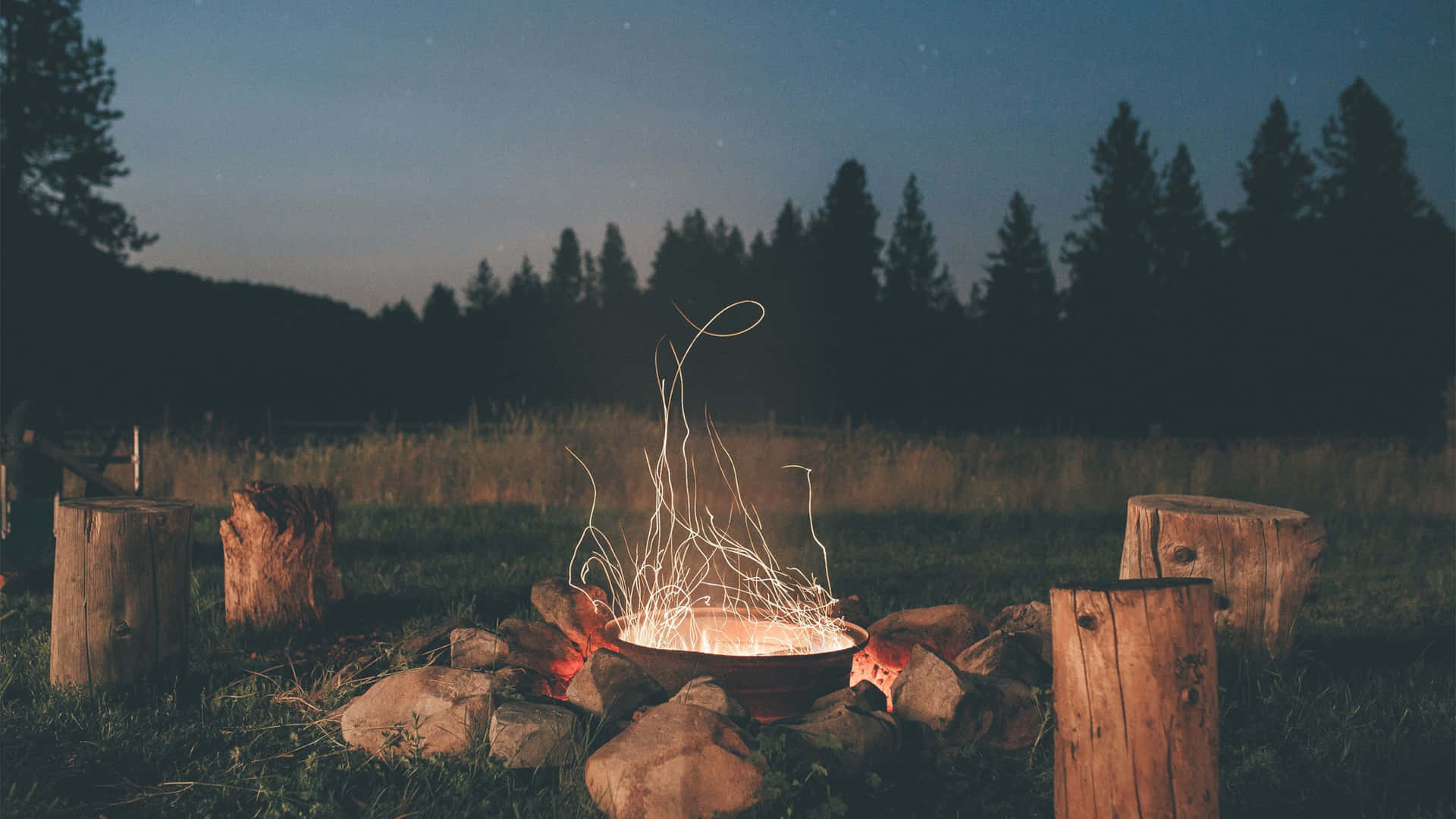 A Campfire In The Middle Of A Field At Night Wallpaper