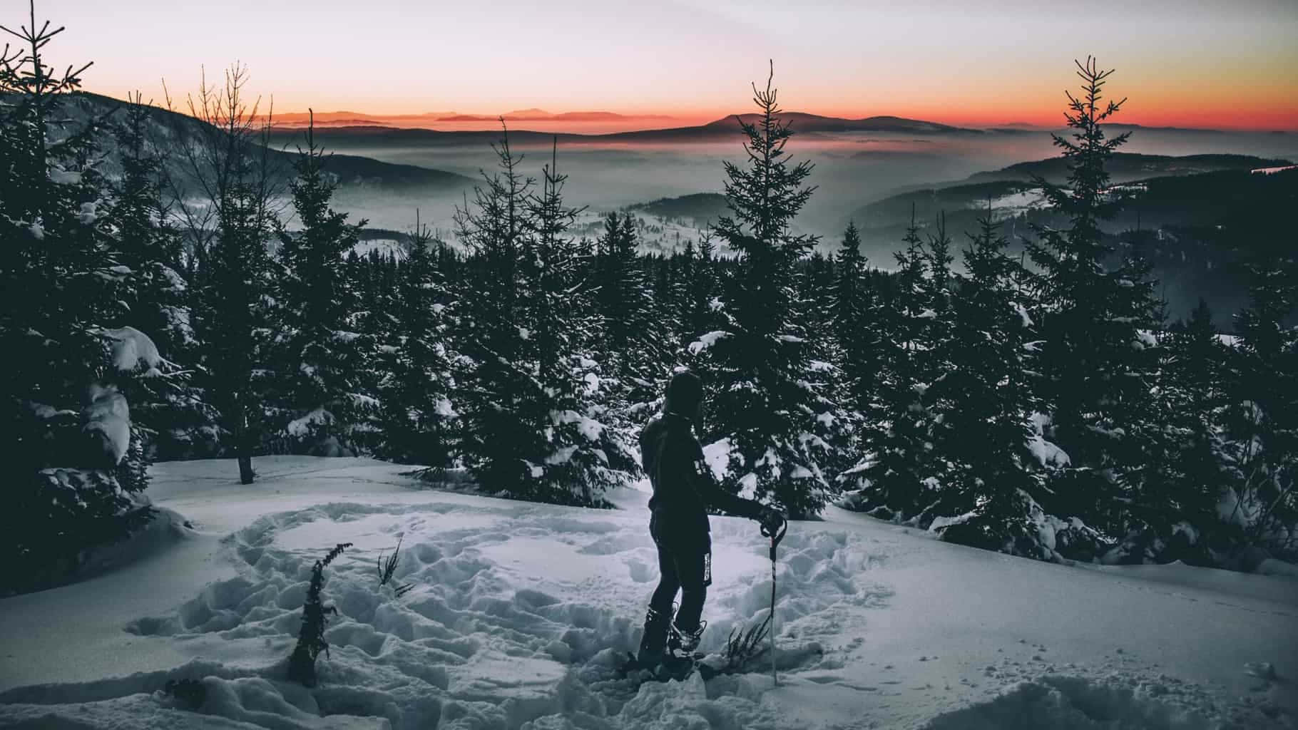 En person står på en sneklædt bjerg ved solnedgang. Wallpaper
